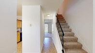 This two-story home in Savage, Maryland offers a practical and well-organized layout spread across two floors. The main level houses the kitchen and living room, while the upper level is dedicated to the two bedrooms, bathroom, and connecting hallways. The kitchen is outfitted with light maple cabinetry, laminate countertops, a stainless steel sink, and white appliances, including a range and dishwasher. A skylight brightens the kitchen, and an adjoining dining area benefits from a large window and an elegant chandelier overhead. The living room features sliding glass doors fitted with vertical blinds, allowing abundant natural light and providing access to the outdoors, where a concrete patio adjoins the brick-and-siding exterior. Upstairs, both bedrooms are carpeted and feature neutral walls and windows that invite natural light. The primary bedroom includes a built-in closet with a full hanging rod. The shared full bathroom is finished with beige ceramic tile surrounding a tub-shower combination, complemented by tile flooring. Hallways on both levels connect the spaces efficiently, with a staircase featuring metal railings linking the two floors. The exterior includes a well-maintained lawn and a paved area alongside the home.