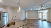 This single-floor unit is designed with a clean, modern aesthetic and an efficient, open layout. The kitchen serves as a central focal point, featuring white shaker-style cabinetry, subway tile backsplash, stainless steel appliances, and a large center island with a quartz countertop and undermount sink. Pendant lighting illuminates the island, while recessed lighting provides additional brightness throughout. The kitchen flows seamlessly into the living area, which is finished with wood-look plank flooring and topped by a ceiling fan. Natural light enters through several windows fitted with horizontal blinds.

Bedrooms are carpeted and offer a calm, neutral palette with natural light from exterior-facing windows. The bathrooms include a well-appointed secondary bath with a tub-shower combo, subway tile surround, white vanity with quartz countertop, and wood-look tile flooring. The primary bath features a walk-in glass-enclosed shower with full subway tile walls and chrome fixtures.

A dedicated laundry room houses a full-size washer and dryer with overhead wire shelving. The private balcony, finished with wood decking and metal railings, provides outdoor access with open views of the surrounding area.