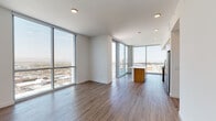 Situated on an upper floor of a high-rise building, this contemporary residence offers an open, airy layout defined by expansive floor-to-ceiling windows that flood the interior with natural light and frame sweeping panoramic city views. Warm hardwood-style flooring runs throughout, creating a cohesive and refined aesthetic.

The open-concept living and dining area flows seamlessly into a well-appointed kitchen, which features a large white quartz island, warm wood cabinetry, a subway tile backsplash, and a full suite of stainless steel appliances including a gas range, microwave, and French door refrigerator. The kitchen's corner window placement provides additional city views, enhancing the sense of openness.

The bedrooms continue the modern design language, with floor-to-ceiling windows, clean white walls, and a notable exposed concrete structural column that adds an industrial accent. One bedroom includes a stylish sliding barn door. The primary bathroom is sleek and well-designed, offering a wood-framed vanity mirror, white quartz countertops, warm wood cabinetry, and a glass-enclosed shower with tile surround. An additional bathroom and a dedicated laundry area with an in-unit washer complete the space. Throughout, recessed lighting and a neutral palette contribute to the clean, contemporary character of this high-rise residence.