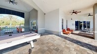 Located at 3305 Grant Cove Circle in Cape Coral, Florida, this outdoor amenity complex offers a resort-style experience designed for relaxation and recreation. At its centerpiece is a generously sized, freeform swimming pool with crystal-clear turquoise water, framed by elegant paver decking and swaying palm trees that reinforce the tropical Florida setting. Ample lounge seating with blue deck chairs is arranged around the pool, providing plenty of space for sunbathing beneath the open sky.

Adjacent to the pool is a covered outdoor pavilion finished with clean white walls, vaulted ceilings, and ceiling fans for comfortable year-round use. This shaded area serves as a social hub, featuring a billiards table, a ping-pong table, cornhole boards, and comfortable lounge seating with vibrant orange accent chairs — making it ideal for both casual gatherings and active recreation.

Large windows along the pavilion's interior walls offer clear sightlines to the pool area, maintaining a seamless indoor-outdoor connection. A decorative pergola structure anchors one side of the pool deck, adding architectural character and additional shade. The multi-story residential buildings surrounding the amenity area complete the community atmosphere, with lush landscaping throughout tying the entire space together into a cohesive, inviting outdoor retreat.