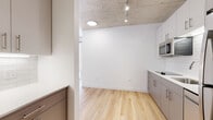 Located in Chicago's vibrant West Town neighborhood, this modern unit at 848 W Eastman St blends industrial character with contemporary finishes. The space is defined by a striking exposed concrete ceiling that adds an urban, loft-inspired aesthetic throughout, complemented by warm light wood flooring that runs continuously across the single floor.

The open kitchen is efficiently designed with taupe gray cabinetry, white subway tile backsplash, light countertops, and a full suite of stainless steel appliances including a refrigerator, dishwasher, microwave, and cooktop. Track lighting mounted to the concrete ceiling illuminates the kitchen and living area, enhancing the clean, modern ambiance.

The living area is bright and open, benefiting from large floor-to-ceiling windows that invite ample natural light and offer views of the surrounding Chicago cityscape and neighboring architecture. The generous glazing creates a strong visual connection to the urban environment outside.

The bathroom features a glass-enclosed walk-in shower lined with classic white subway tile and chrome fixtures, maintaining the clean, minimalist aesthetic found throughout the unit. In-unit laundry is also provided, adding a practical and highly desirable convenience. Overall, the space delivers a cohesive, modern design with quality finishes throughout.