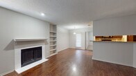 This single-story space offers a cohesive and functional layout with a neutral color palette throughout. The living area serves as the focal point, showcasing rich dark hardwood flooring, a classic tile-surround fireplace with a white mantel, and built-in shelving that provides both storage and display space. Natural light enters through a front-facing window, complementing the recessed lighting overhead. A textured ceiling adds subtle character to the room.

The galley-style kitchen is well-appointed with dark wood cabinetry, granite countertops, a mosaic tile backsplash, and black appliances including a range, microwave, and refrigerator. A stainless steel sink and ample cabinet storage complete the workspace. The kitchen opens toward a dining area illuminated by a pendant light fixture.

The bedrooms are finished with plush neutral carpet and ceiling fans with light kits, creating a comfortable and restful atmosphere. One bedroom includes a window for natural light, while others offer a quieter, more enclosed feel.

The bathroom features dark espresso cabinetry, granite countertops, a large mirror with vanity lighting, hardwood-style flooring, and a full tub-shower combination, providing a clean and updated finish throughout.