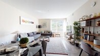 This thoughtfully designed single-floor residence offers a cohesive blend of modern aesthetics and functional living. The open-concept layout connects the living, dining, and kitchen areas seamlessly, creating a spacious and inviting atmosphere throughout.

The living area is bright and airy, benefiting from large windows that invite abundant natural light and offer views of surrounding greenery. Light wood-style flooring runs through the main living spaces, complementing the neutral wall tones. A sliding glass door leads to a private balcony, extending the living space outdoors.

The kitchen is a standout feature, showcasing rich dark cabinetry paired with stainless steel appliances, a classic white subway tile backsplash, under-cabinet lighting, and generous counter space. An island provides additional workspace and casual seating, making it ideal for both everyday cooking and entertaining.

The bedroom is a comfortable retreat, finished with plush carpeting, a large window dressed with sheer curtains, and ample room for furnishings. Soft, neutral tones throughout contribute to a calm and restful environment.

The bathroom is well-proportioned, featuring a long vanity with dual sinks, a wide mirror, white cabinetry, and a full tub-shower combination finished with clean subway tile. Wood-look tile flooring ties the space together with a warm, contemporary feel.