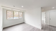 This efficiently laid-out 2-bedroom, 1-bathroom unit offers a clean, modern aesthetic with a cohesive design language carried throughout each room. The interior is finished with light-toned laminate flooring that runs seamlessly across the living areas and bedrooms, complemented by crisp white walls and recessed lighting that enhance the sense of brightness.

The two bedrooms are well-proportioned, each featuring large windows that allow natural light to filter in and offer views of the surrounding neighborhood. The primary bedroom provides a comfortable footprint, while the second bedroom is equally functional. Both rooms include recessed overhead lighting and ample wall space.

The hallway connects the living areas to the bedroom and bathroom, featuring clean lines and white panel doors with matte black hardware — a contemporary detail echoed throughout the unit. The kitchen, visible from the hallway, is equipped with white cabinetry, a stainless steel dishwasher, a stainless steel refrigerator, and a gas range with overhead microwave, all set against a neutral tile backsplash.

The bathroom is finished in an all-white palette with classic hexagonal mosaic floor tiles, a full tub-shower combo with chrome fixtures, and a frosted window that provides natural light while maintaining privacy. The overall ambiance of this unit is modern, clean, and move-in ready.