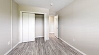 This 2-bedroom, 1-bathroom unit is laid out across a single floor, offering a practical and cohesive floor plan. Consistent grey-toned wood-style flooring runs throughout the entire unit, complemented by neutral beige walls and crisp white trim, creating a clean and modern aesthetic.

The living room is a generous open space featuring a sliding glass door that leads to a private balcony, allowing natural light to fill the room and providing outdoor views. Adjacent to the living area, the galley-style kitchen is well-equipped with white cabinetry, white countertops, a stainless steel sink, and a full suite of appliances including a range, over-the-range microwave, and refrigerator. Recessed and flush-mount lighting illuminates the space efficiently.

The primary bedroom is a well-sized room featuring a window with outdoor views and direct access to the full bathroom. The second bedroom also includes a window for natural light and a built-in closet with sliding doors, offering practical storage. A hallway connects the bedrooms to the shared full bathroom, which includes a single-sink vanity with white cabinetry, a mirror, and a shower/tub combination.