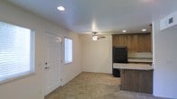 This single-floor space offers a practical and functional layout with a seamlessly connected kitchen and living area. The open-concept design creates an airy feel, with neutral white walls and recessed lighting that brighten the interior throughout the day. A ceiling fan is centrally positioned to ensure comfortable airflow across the main living space.

The kitchen is equipped with warm-toned wooden cabinetry that provides ample storage, complemented by granite-style countertops that add a touch of durability and style. A black refrigerator anchors the kitchen, and a peninsula counter with a raised bar edge extends the workspace while creating a natural division between the kitchen and the living area.

The flooring throughout the space consists of neutral stone-look tile, offering easy maintenance and a cohesive visual flow from room to room. A windowed exterior door allows natural light to filter into the living area, enhancing the bright and open atmosphere. The recessed ceiling lights add to the overall illumination, ensuring the space feels well-lit at any time of day.

Overall, this space presents a clean, no-frills design that emphasizes functionality and ease of living, making it well-suited for everyday comfort and practicality.