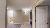 This single-floor residence is designed with a thoughtful layout that balances open communal spaces with well-defined private areas. The living area is a standout feature, boasting soaring vaulted ceilings that amplify the sense of openness, plush carpeting underfoot, and a large picture window that frames verdant outdoor views while drawing in generous natural light. A baseboard heating system runs along the perimeter, ensuring year-round comfort.

The kitchen is positioned adjacent to the living area and is separated by a breakfast bar with granite countertops that doubles as a casual dining space. Light wood cabinetry, stainless steel appliances including a French door refrigerator and range with microwave, and track lighting overhead complete the functional yet attractive cooking space.

A tile-floored hallway, accented with decorative inlays and crown molding, connects the main living areas to the bedrooms. Each bedroom features plush carpeting, crown molding, and windows offering outdoor views. The bathrooms are finished with granite-topped vanities, light wood cabinetry, tile flooring with decorative inlays, and a shower-tub combination. A walk-in closet is accessible from one of the bathrooms, adding convenient storage. Throughout, warm neutral tones and consistent trim work lend the space a cohesive, polished character.