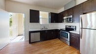 This single-floor residence offers a well-organized layout with a blend of hardwood-style and carpeted flooring throughout. The open-concept living and kitchen area is a central highlight, featuring warm light wood flooring that extends across the generous living space. Large windows along one wall flood the area with abundant natural light while offering views of the surrounding neighborhood and greenery, creating a bright and airy atmosphere.

The kitchen is thoughtfully designed with dark espresso cabinetry providing strong visual contrast against light countertops. Stainless steel appliances, including a refrigerator, range, microwave, and dishwasher, add a modern, functional touch. A window above the sink allows additional natural light into the cooking area.

The bedrooms are finished with plush neutral carpeting, contributing to a quiet and comfortable feel. Each room features windows that bring in natural light and views of the outdoors. Closets with built-in shelving and hanging rods offer practical storage solutions.

The bathroom is clean and functional, featuring light wood-style flooring, a full-sized soaking tub with a tiled shower surround, a dark-finished vanity with a light countertop, and a mirrored medicine cabinet. The overall palette throughout the unit is neutral and bright, lending the space a clean, move-in-ready appeal.