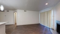 This single-story, one-bedroom, one-bathroom unit offers a thoughtfully organized layout that maximizes its compact footprint. Dark hardwood-style flooring flows consistently throughout, providing a cohesive and modern aesthetic. The combined kitchen and living area serves as the heart of the unit, highlighted by a tile-surround fireplace with glass doors and large vertical blinds that allow natural light to filter in. The kitchen is well-equipped with gray cabinetry, mosaic tile backsplash, black appliances including a refrigerator, range, and built-in microwave, and a peninsula countertop with pendant lighting overhead — ideal for casual dining or food preparation. A textured ceiling adds architectural character across the living spaces. The bedroom is a comfortable, well-proportioned room featuring a ceiling fan with light fixture, a window with blinds, and direct access to a spacious walk-in closet outfitted with dual hanging rods and built-in shelving. The bathroom includes a full tub-shower combination with floor-to-ceiling tile surround. A hallway connects the main living areas, completing this efficiently designed unit.