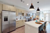 This thoughtfully designed single-floor residence blends contemporary style with everyday functionality. The open-concept kitchen serves as the heart of the home, showcasing light wood cabinetry with matte black hardware, a white quartz countertop, a full suite of stainless steel appliances — including a side-by-side refrigerator with ice maker, electric range, microwave, and dishwasher — and a subway tile backsplash. A central island with built-in open shelving provides additional prep space and casual seating, while bold pendant lighting adds a striking design element overhead. Wood-look flooring flows throughout the main living areas, enhancing the warm, cohesive aesthetic.

The space features two bedrooms, each carpeted and filled with natural light from large windows dressed with sheer curtains and blinds. One bedroom features a teal accent wall, adding a vibrant touch, while the other offers a serene, neutral palette. The bathroom is well-appointed with a wide wood-toned vanity, ample drawer storage, a backlit mirror, a walk-in glass shower, and a tall linen tower for added organization. A dedicated in-unit laundry closet with a stacked washer and dryer rounds out the practical conveniences of this well-equipped residence.