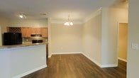 This single-floor space showcases a well-designed open layout that connects the dining area directly to the kitchen, creating a functional and cohesive living environment. The dining area is anchored by a classic multi-bulb chandelier that provides warm, ambient lighting and serves as a subtle focal point. Crown molding runs along the ceiling perimeter, adding a refined architectural detail throughout the space. Rich, dark hardwood flooring extends across the dining and living areas, offering both durability and visual warmth, while crisp white baseboards provide a clean contrast.

The adjacent kitchen features warm-toned maple cabinetry paired with granite countertops and a tiled backsplash, contributing a traditional yet timeless aesthetic. A black range with an overhead microwave completes the kitchen's functional setup. The kitchen is partially separated from the dining area by a raised bar-height counter, which defines each space while maintaining an open, airy feel. Neutral beige walls throughout complement the warm tones of the flooring and cabinetry, creating a cohesive and inviting atmosphere well-suited for everyday living and entertaining.