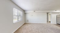 Located at 609 E Pembroke Ave in Hampton, Virginia, Apartment 2C is a single-floor unit designed with a clean, neutral aesthetic throughout. The open living and dining area features plush carpeting, light gray walls, and a bright window with blinds that allows natural light to fill the space. A half-wall with a granite-style countertop separates the living area from the kitchen, adding architectural interest while maintaining an open feel. The kitchen is well-appointed with white shaker-style cabinetry, granite-look countertops, wood-look vinyl flooring, and a full suite of stainless steel appliances including a refrigerator, electric range, and over-the-range microwave. The bedrooms are carpeted and generously sized, each featuring windows for natural light. One bedroom includes a double-door closet, while another offers access to a walk-in closet area. The full bathroom features wood-look vinyl flooring, a white vanity with mirror, and a shower-tub combination. A dedicated utility room houses the water heater and includes wire shelving, providing practical storage. Throughout the unit, consistent white trim and neutral tones create a bright, cohesive atmosphere.