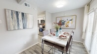 This two-storey residence offers a well-organized layout spread across two levels, combining functional living spaces with contemporary finishes. The main level features a bright living room with vaulted ceilings and a painted brick fireplace as its focal point, complemented by light wood-look flooring that flows throughout. Adjacent to the living area, a dedicated dining space benefits from generous natural light through large windows dressed with blinds and sheer curtains, opening directly into the kitchen. The kitchen is outfitted with white cabinetry, quartz-style countertops, a grey subway tile backsplash, and a full suite of stainless steel appliances including a range, over-the-range microwave, and refrigerator. A half bathroom on the main level provides added convenience for guests, featuring wood-look tile flooring and neutral finishes. Upstairs, the primary bedroom is highlighted by vaulted ceilings and a sliding glass door leading to a private balcony, while a secondary bedroom features plush carpeting, a large window with outdoor views, and mirrored sliding closet doors. A full bathroom with a white vanity and framed mirror serves the upper level. An in-unit laundry area with full-sized washer and dryer adds practical convenience.
