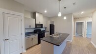 This single-floor residence located on Sherwood Avenue in Holland, Michigan, presents a clean, contemporary design throughout. The open-concept kitchen serves as a functional centerpiece, equipped with black appliances including a range, over-the-range microwave, and refrigerator. Crisp, light-toned cabinetry with matte black hardware contrasts against dark countertops, while a central island with a stainless steel sink provides additional workspace. Two pendant lights hang above the island, enhancing both practicality and visual appeal. Light wood-look flooring extends through the kitchen and living areas, contributing to a bright, cohesive aesthetic.

The living area is generously sized and features sliding glass doors that open to a private balcony, allowing ample natural light and outdoor views. The bedrooms feature neutral carpet, wide windows with blinds, and closets with built-in shelving. The unit includes two bathrooms—one with a tub-shower combination and light flooring, and another featuring a standalone walk-in shower with chrome fixtures. Neutral warm-toned walls throughout unify the space, creating a calm, move-in-ready environment.