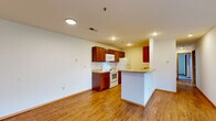 Located at 115 Pin Oak Dr in Aurora, Missouri, this single-floor, 2-bedroom, 2-bathroom home offers a practical and comfortable layout. The open-concept living and dining area flows seamlessly into the kitchen, which features rich wood-toned cabinetry, a granite-look countertop peninsula, recessed lighting, and white appliances including a range, refrigerator, and microwave. Wood-look flooring runs throughout the main living areas, adding warmth and cohesion to the space. The living room is highlighted by a ceiling fan and transitions naturally into the carpeted bedroom hallway. Both bedrooms are carpeted and well-lit, with the primary bedroom offering a generous footprint and its own walk-in closet fitted with wire shelving. A second walk-in closet provides additional storage. The bathrooms include a full tub-shower combination with clean white fixtures. A dedicated laundry room and utility room add everyday convenience. A central hallway connects all rooms efficiently, creating a functional flow throughout the home. Natural light enters through well-placed windows, particularly in the secondary bedroom, which also includes its own closet. Overall, the home presents a clean, straightforward design suited for comfortable single-floor living.