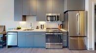 Located at 125 Clifford St in Providence, Rhode Island, this thoughtfully designed studio unit at Emblem 125 offers a seamless open-concept layout that maximizes both function and style. The living and sleeping area is anchored by a large window that frames views of the surrounding neighborhood, flooding the space with natural light. Sheer drape panels and warm hardwood-style flooring contribute to a clean, contemporary aesthetic throughout.

The kitchen is a standout feature, outfitted with flat-front cabinetry in a sophisticated slate-blue and charcoal finish, a white tile backsplash, light quartz countertops, and a full suite of stainless steel appliances including a refrigerator, range, microwave, and dishwasher. A built-in desk with wood surface and open shelving provides a dedicated workspace seamlessly integrated alongside the kitchen, making efficient use of the open floor plan.

The bathroom is finished to a high standard, featuring large-format porcelain tile flooring, a frameless glass walk-in shower with white subway tile surround, a floating vanity with a stone countertop, and neutral wall tones that create a calm, spa-like atmosphere. Every detail of this unit reflects modern urban living at its finest.