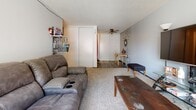 This single-floor unit offers a functional and well-organized layout across several distinct living spaces. The galley-style kitchen is equipped with light wood cabinetry, a tiled backsplash, laminate wood-look flooring, and a full suite of black appliances including a gas range, dishwasher, and refrigerator. Counter space runs along both sides of the corridor-style layout, maximizing utility in a compact footprint.

The living area is carpeted and generously sized, featuring a large sliding glass door that opens to a private balcony, allowing for natural light and outdoor views. A ceiling fan is also present, adding to the room's comfort. The space accommodates both a seating area and a dedicated workspace, highlighting its versatility.

Two carpeted bedrooms provide comfortable personal spaces, each with wall-mounted air conditioning units and baseboard heating for year-round climate control. The rooms offer adequate storage options and connect to the main hallway, which leads to the unit's shared spaces.

The bathroom features classic white tile flooring, a tiled shower and tub combination, a vanity with storage, and clean, neutral finishes throughout. The overall layout of this unit is practical and straightforward, making efficient use of its single-floor design while offering key amenities suited for everyday living.