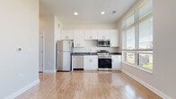 Located at 307 E 1st St in downtown Dayton, Ohio, this single-floor unit offers a clean, contemporary design with a cohesive aesthetic carried throughout each space. Light hardwood-style flooring runs continuously across the unit, contributing to a bright and open atmosphere.

The kitchen is well-appointed with a full suite of stainless steel appliances, including a refrigerator, dishwasher, microwave, and range. White flat-panel cabinetry extends to the ceiling, providing ample storage, while dark countertops offer a subtle contrast. A window positioned beside the kitchen allows natural light to flow into the space.

The living area is generously proportioned, featuring two large windows dressed with blinds that frame views of the surrounding downtown Dayton skyline. The light-filled room benefits from the reflective quality of the flooring, enhancing the sense of openness.

A separate bedroom offers a clean, neutral backdrop with light walls and the same hardwood-style flooring. The bathroom is finished with white cabinetry topped by a dark countertop, an undermount sink, a framed mirror with overhead lighting, and a walk-in shower enclosed by a glass sliding door. Overall, the unit presents a modern and functional living environment in a central urban location.