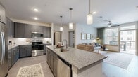 This well-appointed single-floor residence offers a thoughtfully designed open-concept layout that seamlessly connects the kitchen, dining, and living areas. The kitchen is a standout feature, showcasing gray shaker-style cabinetry, granite countertops, a white subway tile backsplash, and a full suite of stainless steel appliances, including a french door refrigerator, range, microwave, and dishwasher. A large central island with pendant lighting overhead provides bar seating for multiple guests, making it ideal for both everyday living and entertaining. The living area is bright and welcoming, benefiting from large windows that invite natural light and offer views of the surrounding exterior. The primary bedroom is a comfortable retreat, featuring a bold accent wall, plush carpeting, a ceiling fan, and generous window coverage with privacy blinds and curtains. It connects directly to the en-suite bathroom, which is outfitted with a granite-topped dual vanity, a framed mirror, and a walk-in glass-enclosed shower with tile surround. The spacious walk-in closet includes built-in shelving and multiple hanging rods for organized storage. A dedicated in-unit laundry room with a full-size washer and dryer and overhead shelving rounds out this functional and stylish residence. Luxury vinyl plank flooring flows throughout the main living areas, adding a cohesive, modern aesthetic.