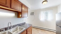 Located at 1401 E Bellows St in Mount Pleasant, Michigan, this single-floor unit offers a practical and well-organized layout. The galley-style kitchen is a standout feature, equipped with rich warm-toned wood cabinetry, dark granite-style countertops, a double stainless steel sink, and black appliances including a refrigerator, electric range, and dishwasher. Tile flooring runs throughout the kitchen and dining area, lending durability and easy maintenance to the high-use spaces. The kitchen opens toward a dining area brightened by a window with vertical blinds and a wall-mounted air conditioning unit, ensuring year-round comfort. Baseboard heating is present throughout the unit, providing consistent warmth during Michigan winters. The bedrooms feature soft carpeting, neutral wall tones, and windows that allow natural light to filter in. One bedroom includes a spacious closet with bi-fold doors and built-in hanging rods, offering ample storage. The overall layout, as seen in the dollhouse view, is elongated and efficiently designed, with clearly defined living, kitchen, and sleeping areas. The light, neutral color palette throughout creates a clean and versatile atmosphere, making the space easy to personalize.