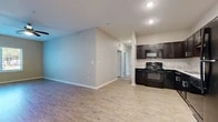 This single-story unit offers a thoughtfully designed open-concept floor plan that connects the living area and kitchen seamlessly. Light wood-look flooring extends throughout the main living spaces, complementing the neutral gray and beige wall tones that create a clean, cohesive aesthetic.

The kitchen is a functional standout, featuring dark espresso cabinetry with brushed silver hardware, light-toned countertops with a subtle tile backsplash, and a full suite of black appliances including a range, built-in microwave, dishwasher, and refrigerator. Recessed lighting illuminates the space effectively. The open layout allows the kitchen to flow naturally into the living area, which provides ample room for furniture arrangement.

The bedrooms are well-proportioned, each finished with the same wood-look flooring. Bedrooms feature windows with outdoor views of landscaped greenery, allowing natural light to filter in. Closets with built-in rods offer practical storage solutions.

The bathrooms feature full-size soaking tubs and shower surrounds in clean white finishes, with tile flooring providing a crisp contrast. A dedicated laundry area with hookups adds convenience. Overall, the unit presents a modern, move-in-ready interior with consistent finishes throughout.