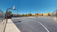 Located at 2895 E Charleston Blvd in Las Vegas, Nevada, this outdoor recreational facility features a well-maintained sports complex designed to serve the surrounding community. The centerpiece is a spacious full-length basketball court, complete with clearly painted court markings, key areas, and multiple hoops with regulation backboards positioned at each end. The court surface is finished in smooth asphalt, providing a consistent playing area suited for both casual play and organized games.

Adjacent to the basketball court is a tennis court, also asphalt-surfaced and clearly lined, enclosed within sturdy chain-link fencing that defines each playing area and ensures safety. Tall pole-mounted floodlights are distributed throughout the complex, enabling use during evening hours. The perimeter fencing around the entire facility offers a secure, dedicated recreational environment.

Surrounding the courts, mature trees provide natural shade and greenery, softening the hardscape environment. Views from the courts reveal nearby residential buildings with Spanish-style rooflines, desert landscaping with shrubs and ground cover, and glimpses of a pool area visible from within the complex. Ample parking is accessible directly adjacent to the facility. Under the wide-open Las Vegas sky, this sports complex offers a functional and inviting destination for athletic activity year-round.