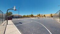 Located at 2895 E Charleston Blvd in Las Vegas, Nevada, this outdoor recreational facility features a well-maintained sports complex designed to serve the surrounding community. The centerpiece is a spacious full-length basketball court, complete with clearly painted court markings, key areas, and multiple hoops with regulation backboards positioned at each end. The court surface is finished in smooth asphalt, providing a consistent playing area suited for both casual play and organized games.

Adjacent to the basketball court is a tennis court, also asphalt-surfaced and clearly lined, enclosed within sturdy chain-link fencing that defines each playing area and ensures safety. Tall pole-mounted floodlights are distributed throughout the complex, enabling use during evening hours. The perimeter fencing around the entire facility offers a secure, dedicated recreational environment.

Surrounding the courts, mature trees provide natural shade and greenery, softening the hardscape environment. Views from the courts reveal nearby residential buildings with Spanish-style rooflines, desert landscaping with shrubs and ground cover, and glimpses of a pool area visible from within the complex. Ample parking is accessible directly adjacent to the facility. Under the wide-open Las Vegas sky, this sports complex offers a functional and inviting destination for athletic activity year-round.