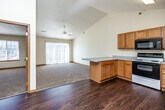 This single-floor unit is designed with an open-concept layout that seamlessly connects the kitchen and living areas. The kitchen is well-equipped with warm honey-toned oak cabinetry, a full suite of appliances including an electric range, built-in microwave, dishwasher, and refrigerator, along with a peninsula counter that provides additional workspace and separation between the kitchen and adjoining areas. The flooring in the kitchen transitions from rich dark hardwood to plush neutral carpet in the living space.

The living area benefits from vaulted ceilings that lend a sense of openness and volume, complemented by a ceiling fan overhead. A sliding glass door floods the space with natural light and provides exterior access. The overall color palette is neutral throughout, featuring cream walls and warm wood trim.

The bedrooms are carpeted and generously sized, each featuring windows for natural light. At least one bedroom includes a closet with bifold doors. The bathroom is finished with oak cabinetry, a wide vanity with a white countertop, hardwood-style flooring, and a full tub-shower combination. The unit's layout and finishes provide a clean, functional, and comfortable living environment.
