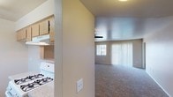 This single-story residence features a practical and functional layout with a neutral color palette of warm beige tones throughout. The expansive living room is a standout space, showcasing plush carpeting, a ceiling fan with integrated lighting, and generous natural light admitted through large windows dressed with vertical blinds. A sliding door provides additional light and outdoor access. The kitchen is partially separated from the living area by a half-wall partition, and includes a gas range, overhead ventilation, and light wood cabinetry with ample counter space.

The multiple bedrooms continue the carpeted flooring and warm beige walls, each benefiting from large windows with vertical blinds that allow for abundant natural light. The rooms offer versatile, open layouts suitable for various furniture configurations.

The two bathrooms each feature a full tub-and-shower combination with white tile surrounds and chrome fixtures. One bathroom is appointed with wood-look vinyl flooring, a wood-toned vanity, and a granite-patterned countertop, providing a more refined finish. The second bathroom also features wood-look vinyl flooring, maintaining a cohesive design. Together, the spaces offer a clean, understated aesthetic well-suited for comfortable everyday living.
