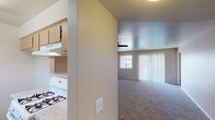 This single-story residence features a practical and functional layout with a neutral color palette of warm beige tones throughout. The expansive living room is a standout space, showcasing plush carpeting, a ceiling fan with integrated lighting, and generous natural light admitted through large windows dressed with vertical blinds. A sliding door provides additional light and outdoor access. The kitchen is partially separated from the living area by a half-wall partition, and includes a gas range, overhead ventilation, and light wood cabinetry with ample counter space.

The multiple bedrooms continue the carpeted flooring and warm beige walls, each benefiting from large windows with vertical blinds that allow for abundant natural light. The rooms offer versatile, open layouts suitable for various furniture configurations.

The two bathrooms each feature a full tub-and-shower combination with white tile surrounds and chrome fixtures. One bathroom is appointed with wood-look vinyl flooring, a wood-toned vanity, and a granite-patterned countertop, providing a more refined finish. The second bathroom also features wood-look vinyl flooring, maintaining a cohesive design. Together, the spaces offer a clean, understated aesthetic well-suited for comfortable everyday living.