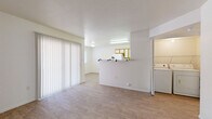 Located at 1501 S Highway 79 in Florence, Arizona, this single-floor 2-bedroom, 1-bathroom residence offers a practical and well-organized layout. The living area is bright and open, featuring light wood-style flooring throughout and large vertical-blind sliding doors that allow natural light to fill the space. A half-wall divides the living area from the kitchen, creating a semi-open feel while maintaining defined zones. The U-shaped kitchen is equipped with white appliances including a range, refrigerator, and dishwasher, complemented by wood-trimmed cabinetry with white panels and ample counter space. Both bedrooms are generously proportioned with wood-style flooring, bright white walls, and windows fitted with horizontal blinds that provide natural light and privacy. The primary bedroom is notably spacious. The full bathroom includes a tub-shower combo, a single-sink vanity with wood-trimmed cabinetry, and a large mirror. The home also features three closets for abundant storage, a dedicated laundry area, and a hallway connecting the main living spaces. The consistent light-toned flooring and clean white walls throughout create a cohesive, airy atmosphere across the entire residence.