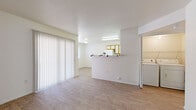 Located at 1501 S Highway 79 in Florence, Arizona, this single-floor 2-bedroom, 1-bathroom residence offers a practical and well-organized layout. The living area is bright and open, featuring light wood-style flooring throughout and large vertical-blind sliding doors that allow natural light to fill the space. A half-wall divides the living area from the kitchen, creating a semi-open feel while maintaining defined zones. The U-shaped kitchen is equipped with white appliances including a range, refrigerator, and dishwasher, complemented by wood-trimmed cabinetry with white panels and ample counter space. Both bedrooms are generously proportioned with wood-style flooring, bright white walls, and windows fitted with horizontal blinds that provide natural light and privacy. The primary bedroom is notably spacious. The full bathroom includes a tub-shower combo, a single-sink vanity with wood-trimmed cabinetry, and a large mirror. The home also features three closets for abundant storage, a dedicated laundry area, and a hallway connecting the main living spaces. The consistent light-toned flooring and clean white walls throughout create a cohesive, airy atmosphere across the entire residence.