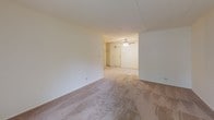 Located at 1503 W Hintz Rd in Wheeling, Illinois, this single-floor unit offers a practical and comfortable layout with several notable features throughout. The main living area is generously proportioned, finished with neutral wall-to-wall carpeting and crisp white walls that create a clean, bright atmosphere. A sliding glass door floods the space with natural light and provides views of the lush greenery outside, while a wall-mounted heating unit ensures year-round comfort. The living area flows into a secondary carpeted space equipped with a ceiling fan and access to a built-in closet, offering flexible use as a dining area or additional room. The kitchen features a striking contrast of dark cabinetry with gold-toned hardware set against light countertops, complemented by a double stainless steel sink, electric cooktop, and white refrigerator. Light tile flooring completes the functional cooking space. The bedroom is a comfortable retreat with plush carpeting, a spacious closet with sliding doors, and direct access to the full bathroom. The bathroom is finished with tile flooring in a mosaic pattern, a single vanity with a large mirror and lighted fixture above, and a tiled tub and shower combination. Large windows throughout the unit invite natural light and offer pleasant outdoor views of the surrounding landscape.