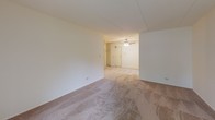 Located at 1503 W Hintz Rd in Wheeling, Illinois, this single-floor unit offers a practical and comfortable layout with several notable features throughout. The main living area is generously proportioned, finished with neutral wall-to-wall carpeting and crisp white walls that create a clean, bright atmosphere. A sliding glass door floods the space with natural light and provides views of the lush greenery outside, while a wall-mounted heating unit ensures year-round comfort. The living area flows into a secondary carpeted space equipped with a ceiling fan and access to a built-in closet, offering flexible use as a dining area or additional room. The kitchen features a striking contrast of dark cabinetry with gold-toned hardware set against light countertops, complemented by a double stainless steel sink, electric cooktop, and white refrigerator. Light tile flooring completes the functional cooking space. The bedroom is a comfortable retreat with plush carpeting, a spacious closet with sliding doors, and direct access to the full bathroom. The bathroom is finished with tile flooring in a mosaic pattern, a single vanity with a large mirror and lighted fixture above, and a tiled tub and shower combination. Large windows throughout the unit invite natural light and offer pleasant outdoor views of the surrounding landscape.