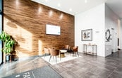 The lobby of The Fairmount at McKinley Square, located at 728 Bergen Ave in Jersey City, NJ, presents a polished and contemporary first impression. The entrance features floor-to-ceiling glass panels and double doors that allow natural light to filter into the space, with views of the surrounding streetscape. Large-format dark tile flooring extends throughout, lending a cohesive, sophisticated foundation to the entire area.

Upon entry, a welcoming lounge area is defined by a textured area rug and anchored by a marble-topped round coffee table surrounded by curved cognac leather chairs. A rich wood-paneled accent wall serves as a focal point, with a wall-mounted digital display screen providing building information. The warm tones of the wood paneling contrast elegantly with the cool grey walls found throughout the rest of the lobby.

The corridor leading to the elevators is lined with curated abstract artwork, adding an artistic dimension to the functional space. Industrial-style pendant lighting illuminates the hallway, creating a well-lit path to the stainless steel elevator banks. Minimalist black benches offer additional seating along the walls. The overall ambiance is modern, clean, and professional, reflecting a well-maintained residential building.
