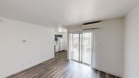 This studio in Austin, TX offers an efficiently designed single-floor layout that combines the living and kitchen areas into one cohesive open space. Dark wood-style laminate flooring runs throughout, providing a warm contrast against the crisp white walls and ceilings. The main living area is bright and open, benefiting from a large sliding glass door fitted with vertical blinds that allows natural light to filter in and provides direct access to an outdoor area with exterior views. A wall-mounted split A/C unit ensures year-round climate control.

The kitchen is positioned at the rear of the main space and features gray cabinetry with brushed nickel hardware, a marble-look countertop, a stainless steel sink, and a white electric coil range with an overhead ventilation hood. A white refrigerator and dishwasher complete the kitchen appliance package, making the space fully functional despite its compact footprint.

The bathroom is clean and well-appointed, featuring a full tub-shower combination with a white surround, a toilet, and a vanity with a marble-patterned countertop and single basin sink. The consistent use of white tones throughout the bathroom creates a bright, tidy atmosphere. Overall, this studio presents a practical and neatly finished living space in northeast Austin.