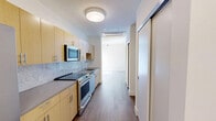 Located on the 15th floor at 42 Broad St W in Mount Vernon, NY, Unit 1501 is a thoughtfully designed one-bedroom, one-bathroom residence that makes efficient use of its compact footprint. The galley-style kitchen is outfitted with light wood cabinetry, stainless steel appliances including a range and built-in microwave, a marble-style tile backsplash, and a dark countertop that adds a modern contrast. Warm hardwood-style flooring runs throughout the unit, complementing the clean, white walls and creating a cohesive, contemporary aesthetic. The hallway entry leads seamlessly into the living and sleeping areas, with the layout maximizing functionality. The generously sized bedroom, comprising roughly half the unit's total area, features large windows that invite natural light and offer elevated outdoor views of the surrounding neighborhood. The bathroom is finished to a high standard, featuring a walk-in shower clad in large-format marble-look porcelain tiles, a mosaic tile floor, chrome fixtures, and a wood-toned vanity with a clean white countertop and a recessed medicine cabinet mirror. The overall ambiance of the unit is bright, modern, and move-in ready, with consistent finishes throughout that reflect quality craftsmanship.