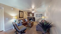 Located at 4700 N Kolb Rd in Tucson, Arizona, this single-story residence offers a thoughtfully arranged layout with a warm, inviting atmosphere throughout. The living room serves as the focal point of the home, anchored by a fireplace set against a striking wood-paneled accent wall. A ceiling fan overhead and neutral-toned carpet underfoot create a comfortable setting, while the open sightline to the kitchen keeps the space feeling connected and airy. The room accommodates a generous seating arrangement, ideal for both relaxing and entertaining.

The home features two bedrooms, each finished with plush carpet and ceiling fans. The primary bedroom is spacious enough for a substantial furniture suite and benefits from natural light through large windows. The second bedroom offers a similarly comfortable feel, with easy access to a closet and adjacent bathroom. Both rooms maintain a calm, neutral palette that complements the overall tone of the home.

The bathrooms are practical and well-lit, featuring wide vanity countertops, large mirrors with overhead lighting, and a combination tub and shower with glass-panel enclosures. Glass block windows allow natural light to filter in while maintaining privacy. Wood-look flooring in the bathrooms adds a warm contrast to the light-colored cabinetry and countertops throughout.