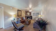 Located at 4700 N Kolb Rd in Tucson, Arizona, this single-story residence offers a thoughtfully arranged layout with a warm, inviting atmosphere throughout. The living room serves as the focal point of the home, anchored by a fireplace set against a striking wood-paneled accent wall. A ceiling fan overhead and neutral-toned carpet underfoot create a comfortable setting, while the open sightline to the kitchen keeps the space feeling connected and airy. The room accommodates a generous seating arrangement, ideal for both relaxing and entertaining.

The home features two bedrooms, each finished with plush carpet and ceiling fans. The primary bedroom is spacious enough for a substantial furniture suite and benefits from natural light through large windows. The second bedroom offers a similarly comfortable feel, with easy access to a closet and adjacent bathroom. Both rooms maintain a calm, neutral palette that complements the overall tone of the home.

The bathrooms are practical and well-lit, featuring wide vanity countertops, large mirrors with overhead lighting, and a combination tub and shower with glass-panel enclosures. Glass block windows allow natural light to filter in while maintaining privacy. Wood-look flooring in the bathrooms adds a warm contrast to the light-colored cabinetry and countertops throughout.