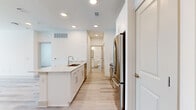 This efficiently designed single-floor residence offers a bright, modern living experience through a clean, neutral palette and quality finishes throughout. The open-concept kitchen and living area forms the heart of the home, anchored by a striking peninsula with a granite-style stone countertop, an undermount sink, and crisp white shaker cabinetry. A full suite of stainless steel appliances — including a French door refrigerator, range, and microwave — completes the kitchen. Light wood-look flooring runs throughout the main living areas, enhancing the airy, cohesive feel of the space. A full-glass exterior door floods the living area with natural light. The spacious bedroom features soft carpeting, a ceiling fan, and direct access to both the bathroom and a dedicated walk-in closet outfitted with double hanging rods and shelving. The bathroom maintains the home's clean aesthetic with a white vanity, granite-topped countertop, a framed mirror, and stylish chrome light fixtures. Recessed lighting throughout ensures consistent, comfortable illumination across every room. The overall ambiance is contemporary and move-in ready, offering a streamlined and functional living environment.