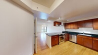 This 2-bedroom, 2-bathroom residence is laid out across a single floor, offering a cohesive and functional living environment. The open-concept kitchen and living area serves as the heart of the home, featuring warm bamboo hardwood flooring throughout. The kitchen is well-equipped with rich cherry wood cabinetry, dark granite countertops, stainless steel appliances including a built-in microwave and refrigerator, and a peninsula island that provides additional prep space and a natural divider between the kitchen and living area. The living room is bright and airy, benefiting from large sliding glass doors that open onto a private balcony with views of the surrounding cityscape. Both bedrooms are generously sized and finished with plush carpeting for added comfort. The spacious primary bedroom includes a closet and ample room for furnishings. The two bathrooms are consistently finished with gray tile flooring, dark wood vanities, and granite countertops. A dedicated hallway connects the living spaces to the private quarters, contributing to a well-organized floor plan. Recessed lighting and large windows ensure the residence is filled with natural light throughout.
