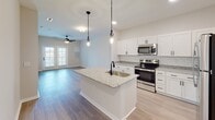 Located at 6080 Tides Way in Myrtle Beach, SC, this well-appointed single-floor home offers a clean, modern aesthetic throughout. The open-concept kitchen serves as the heart of the home, showcasing crisp white shaker cabinetry, a classic subway tile backsplash, and granite countertops that extend onto a central island with an undermount sink and striking matte black pendant lighting overhead. Stainless steel appliances, including a range, microwave, and refrigerator, complete the kitchen's functional and stylish design. The kitchen flows seamlessly into the living area, which features durable wood-look flooring, a ceiling fan, and generous natural light streaming through sliding glass doors — creating a bright, airy atmosphere. The bedrooms are carpeted for comfort and include ceiling fans and windows that bring in additional natural light with views of the surrounding neighborhood. The bathroom is finished with granite-topped vanity cabinetry and light wood-look flooring, maintaining the home's cohesive, neutral palette. A spacious walk-in closet with wire shelving provides ample storage. Throughout the home, neutral tones, recessed lighting, and consistent finishes create a polished and inviting living environment ideal for the Myrtle Beach lifestyle.