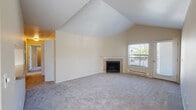 This single-level residence is defined by its striking vaulted ceilings in the main living area, which lend a sense of volume and openness to the space. The living room centers around a classic fireplace with a white-trimmed mantle, flanked by a window and a door providing access to an outdoor balcony, allowing natural light to fill the room. Neutral-toned carpet runs throughout the living and bedroom areas, contributing to a cohesive and understated aesthetic.

A pass-through opening connects the living area to the galley-style kitchen, which features white cabinetry with light wood trim, laminate countertops, wood-look flooring, and white appliances including a range, dishwasher, and refrigerator. The layout is efficient and well-organized.

The bedrooms are carpeted and finished in warm neutral tones, each with windows that bring in natural light. At least one bedroom includes a reach-in closet with sliding doors and a baseboard heater. The bathrooms feature wood-look tile flooring, extended vanity countertops, under-sink cabinetry, and large mirrors, offering a functional and clean design throughout.