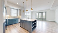 This well-appointed single-floor residence showcases a cohesive modern design with light wood flooring, crisp white walls, and sage green trim and door accents throughout. The open-concept kitchen is a standout feature, offering two-tone cabinetry with blue-gray lower cabinets and white upper cabinets, a large central island with built-in shelving, a white quartz countertop, and stainless steel appliances. Three gold pendant lights hang above the island, adding a warm, contemporary touch. The kitchen flows naturally into a spacious living area bathed in natural light from a set of French doors and multiple windows. The bedrooms are generously sized, each featuring light wood flooring, ceiling fans, and windows that allow ample natural light to fill the rooms. Closet options include walk-in configurations with built-in shelving and hanging rods, as well as reach-in closets with bifold doors. The bathrooms are distinctively designed with terracotta hexagonal floor tiles, blue-gray vanity cabinetry, white subway tile walls, and white quartz countertops. One bathroom features a double vanity with a walk-in glass shower, while another offers a full tub-shower combo. The overall ambiance is clean, bright, and modern, with thoughtful design details that create a cohesive and inviting living space.