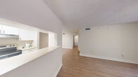 This well-appointed one-bedroom, one-bathroom unit at 6460 Main St offers a thoughtfully designed single-floor layout that maximizes every square foot. The open-concept living and dining area is bathed in natural light, showcasing warm wood-look flooring that flows throughout the main living spaces. A sliding glass door leads to a private balcony, seamlessly connecting the interior to the outdoors. The kitchen features a convenient pass-through window into the living area, white cabinetry, light tile flooring, stainless steel appliances including a refrigerator and range, and ample counter space — all illuminated by overhead lighting. A hallway connects the living area to the private quarters. The generously sized bedroom includes a ceiling fan with light fixture, a window with natural light, and direct access to a spacious walk-in closet outfitted with wire shelving on multiple levels for excellent storage. The full bathroom offers a tiled tub-shower combination, toilet, and vanity sink with tile flooring. Textured ceilings are featured throughout, adding a classic touch. The unit also includes in-unit laundry hookups, visible in the hallway area, adding a practical convenience to this comfortable and functional home.
