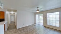 This single-floor residence offers a well-organized layout with light-filled living spaces and consistent wood-look flooring throughout. The main living area is bright and open, featuring a ceiling fan with integrated lighting, sliding glass doors that lead to a private balcony with outdoor views, and vertical blinds that allow for flexible light control. A second living or dining area mirrors this design with its own ceiling fan, a large window, and direct access to the front entry door.

The kitchen is efficiently laid out in an L-shape, equipped with warm-toned wood cabinetry, white countertops, a double stainless steel sink, a black electric range with overhead ventilation, and a built-in dishwasher. Upper shelving provides additional storage options.

The bedrooms are comfortably sized, each benefiting from natural light through windows with blinds. One bedroom features a roomy walk-in closet outfitted with multiple shelving tiers and hanging rods, while another includes a broad bifold-door closet with a full-width hanging rod.

Two full bathrooms are present, each featuring a clean, white tub-shower surround with chrome fixtures and a toilet. The overall aesthetic of the space is clean and neutral, with white walls, light flooring, and a bright, airy ambiance throughout.