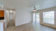 This single-floor residence offers a well-organized layout with light-filled living spaces and consistent wood-look flooring throughout. The main living area is bright and open, featuring a ceiling fan with integrated lighting, sliding glass doors that lead to a private balcony with outdoor views, and vertical blinds that allow for flexible light control. A second living or dining area mirrors this design with its own ceiling fan, a large window, and direct access to the front entry door.

The kitchen is efficiently laid out in an L-shape, equipped with warm-toned wood cabinetry, white countertops, a double stainless steel sink, a black electric range with overhead ventilation, and a built-in dishwasher. Upper shelving provides additional storage options.

The bedrooms are comfortably sized, each benefiting from natural light through windows with blinds. One bedroom features a roomy walk-in closet outfitted with multiple shelving tiers and hanging rods, while another includes a broad bifold-door closet with a full-width hanging rod.

Two full bathrooms are present, each featuring a clean, white tub-shower surround with chrome fixtures and a toilet. The overall aesthetic of the space is clean and neutral, with white walls, light flooring, and a bright, airy ambiance throughout.
