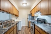This 2-bedroom, 1-bathroom residence is thoughtfully laid out across a single floor, making efficient use of its space. The open living room features warm wood-look vinyl flooring, clean white walls, and a ceiling fan with a light fixture, creating a bright and airy atmosphere. The layout connects seamlessly to the galley-style kitchen, which is equipped with warm wood cabinetry, dark granite-style countertops, a double stainless steel sink, and a black electric range — providing ample storage and prep space along both sides of the corridor. The full bathroom includes a wood-toned vanity with a granite-style countertop, a large mirror, a baseboard heater, and a separate shower area. Both bedrooms are carpeted and offer a comfortable, cozy feel, with the primary bedroom featuring a large window that allows natural light to flow through. Each bedroom is serviced by its own closet for added storage. A hallway connects the private areas of the home to the main living spaces. Consistent wood-look flooring runs throughout the common areas, tying the home together with a cohesive, functional aesthetic suited for everyday living.
