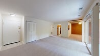This single-floor residence offers a thoughtfully laid-out living space with a clean, neutral palette throughout. The generously sized living area is carpeted in light grey and features louvered double doors for additional storage. An open sightline connects the living space to the kitchen and a separate dining or entry area, which is distinguished by a warm exposed brick accent wall and overhead beam detail, adding architectural character to the otherwise contemporary interior.

The kitchen is efficiently designed and equipped with warm-toned wooden cabinetry, dark laminate countertops, a gas range, dishwasher, refrigerator, and a built-in microwave. A stainless steel sink sits beneath upper cabinets, one of which features a glass-front panel, and the kitchen benefits from its own tile flooring.

The bedrooms are carpeted and bright, each featuring louvered bifold closet doors with built-in rods and shelving for organized storage. One bedroom includes a window with views of a neighboring structure, while the main living area opens via sliding glass doors to a private balcony overlooking lush, mature trees. The bathroom is finished with white tile surrounds and a full tub-shower combination, maintaining a clean and functional aesthetic throughout.