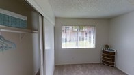 This single-floor residential unit offers a clean, functional layout designed with everyday comfort in mind. The bedroom is a standout feature, showcasing a generously sized sliding-door closet that provides ample storage space. A large picture window fills the room with natural light while framing a pleasant outdoor view of surrounding greenery and neighboring buildings, creating a bright and welcoming atmosphere. The room is finished with wall-to-wall carpeting that adds warmth underfoot, and neutral, light-toned walls lend a sense of openness throughout. The textured popcorn ceiling is consistent across the space, adding a classic residential character. Vertical window treatments offer privacy while maintaining the flow of natural light. The overall ambiance is simple, tidy, and practical, making it a comfortable and versatile living space. The neutral color palette throughout ensures the space is adaptable to a variety of interior styles and furnishing preferences, while the natural light and garden-facing window contribute to an airy, refreshing feel within the home.